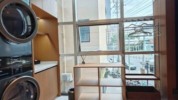 A compact kitchen with a built-in washer and dryer, a window with a view of the city, and a small wooden shelf unit.