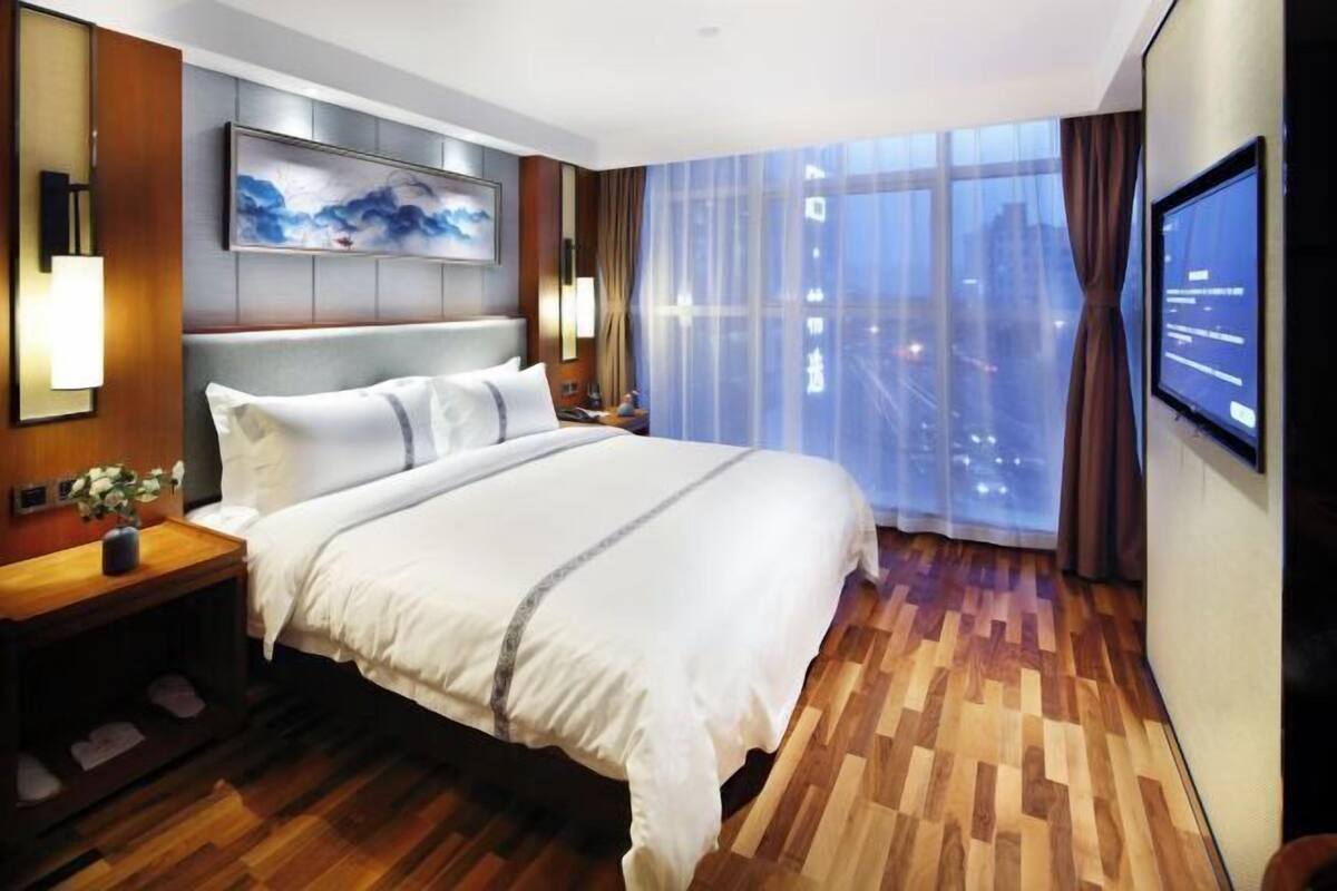A modern hotel room with a large bed, a city view, and a flat-screen TV.