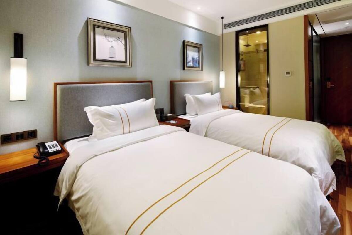 A hotel room with two beds, a bedside table with a phone, and framed artwork on the wall.