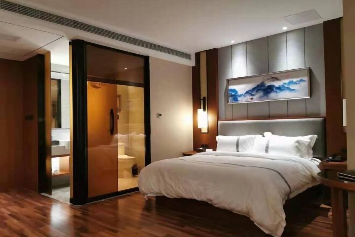 A modern hotel room with a bed, a painting on the wall, and a sliding door leading to a bathroom.