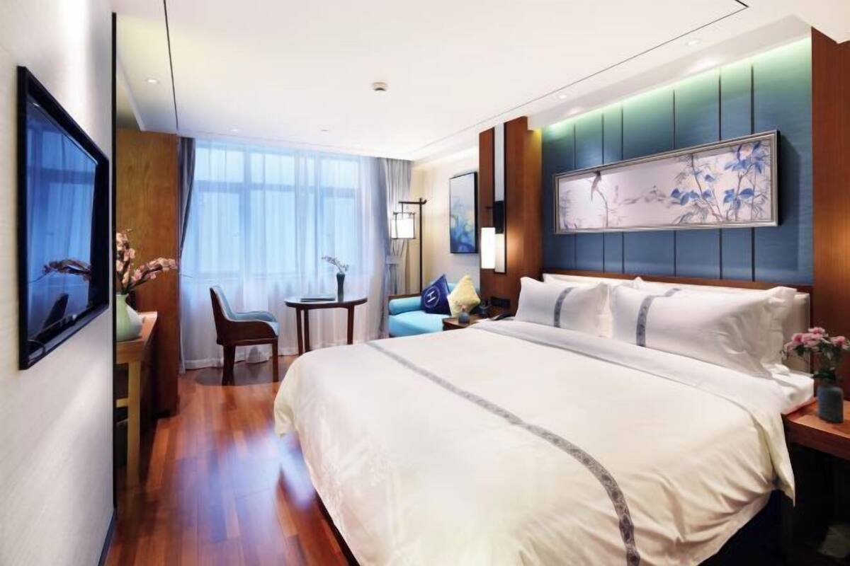 A hotel room with a large bed, a desk, a chair, a small table, and a painting on the wall.