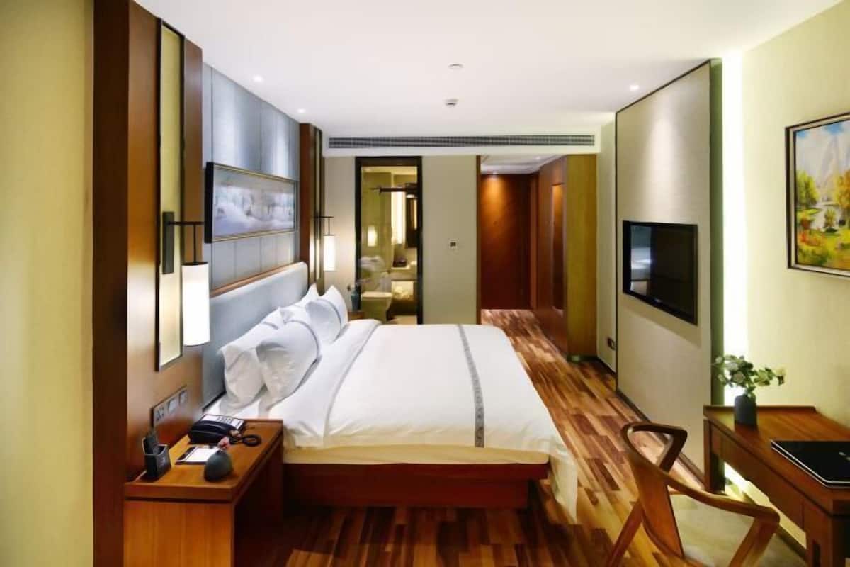 A hotel room with a large bed, a desk with a chair, a TV, and a painting on the wall.
