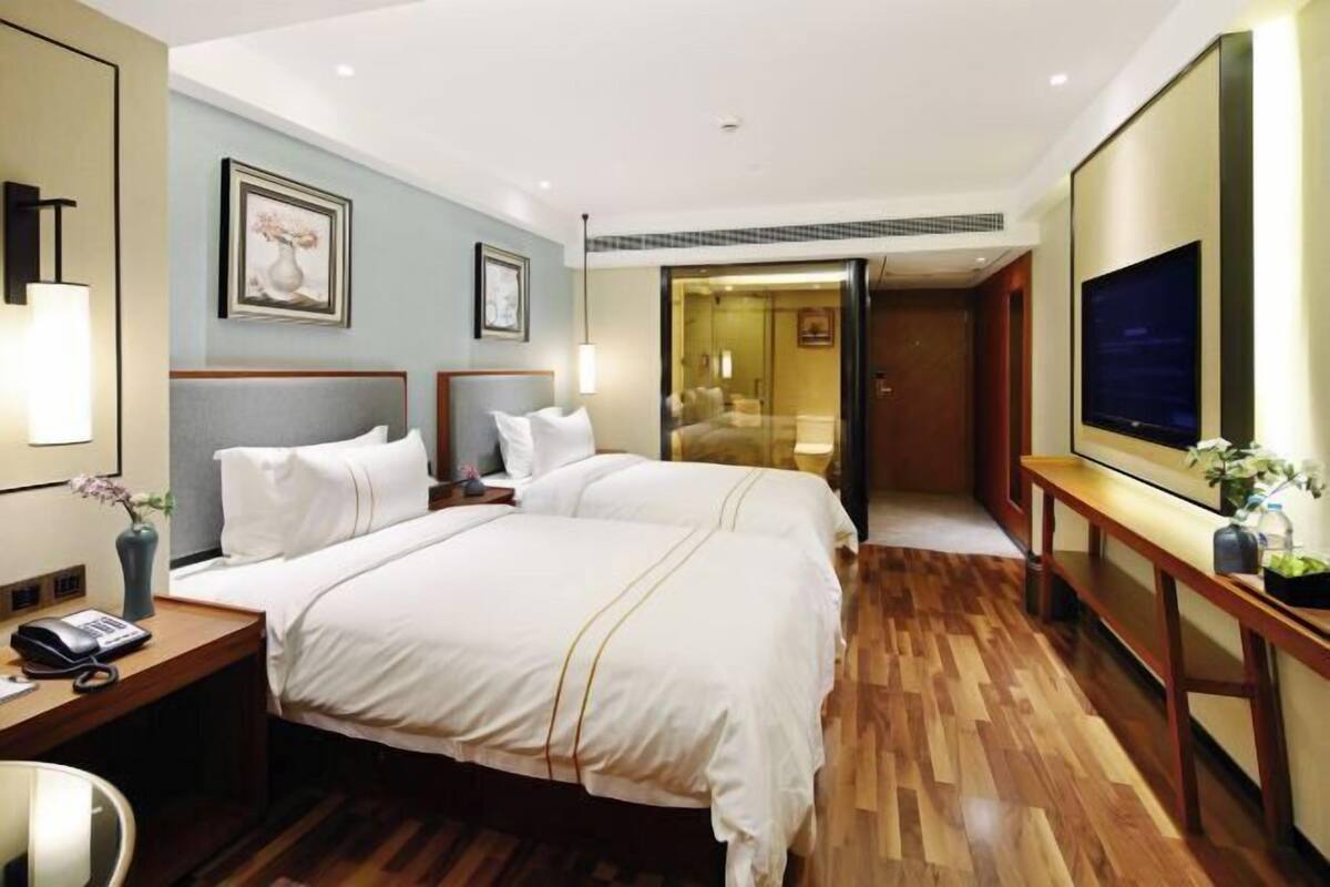 A hotel room with two beds, a desk with a telephone, a TV, and a door leading to a bathroom.