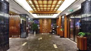 Un vestíbul d'hotel modern amb sòl de marbre, detalls de fusta i plantes en testos.