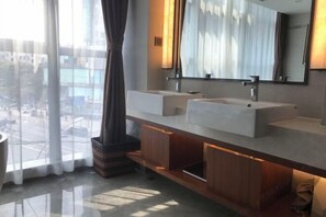 Un baño moderno con dos lavamanos, un espejo grande y vistas a un paisaje urbano a través de amplios ventanales.