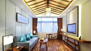 Habitació d'hotel moderna amb sostre de fusta, un sofà amb coixins, una taula rodona petita, una televisió i una finestra amb cortines.