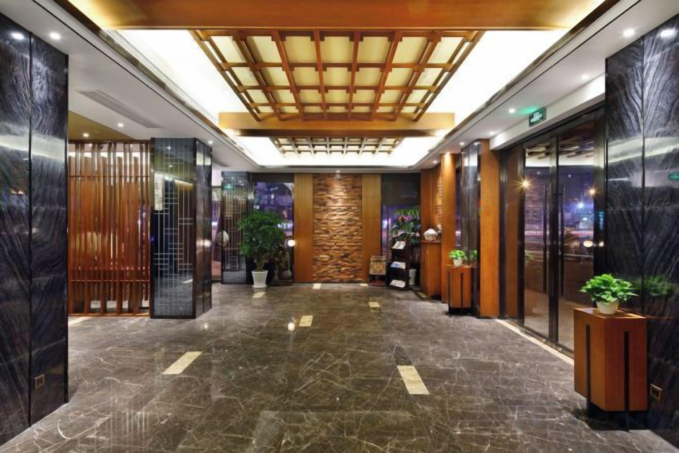 A hotel lobby with a central column, a ceiling with a wooden panel design, and a marble floor.