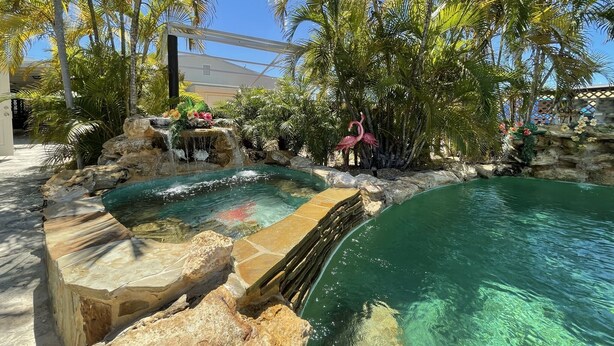 A pool area with a waterfall, palm trees, and a pink flamingo statue. - BEST House in Marathon With Ocean View! (Marathon)