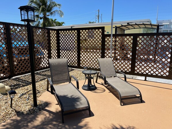 A patio area with two lounge chairs and a small table, surrounded by a lattice fence. - BEST House in Marathon With Ocean View! (Marathon)