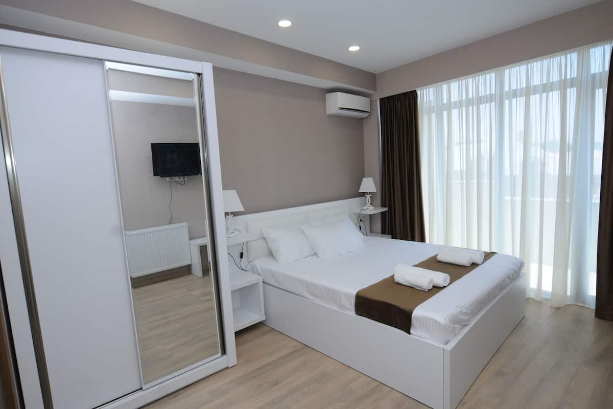 A modern hotel room with a large bed, a TV, an air conditioning unit, and a window with curtains.