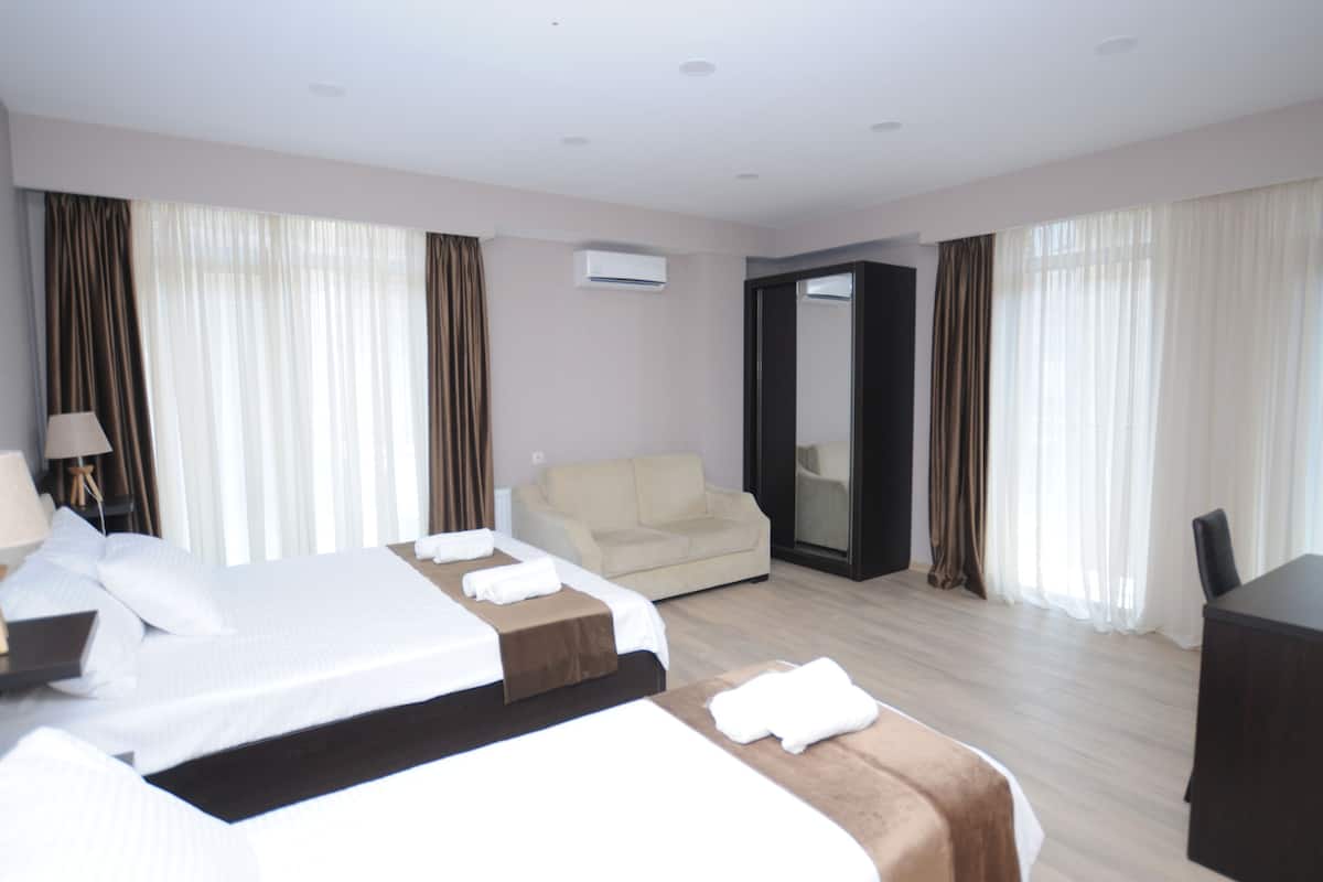 A hotel room with a large bed, a sofa, a desk, and a mirror.