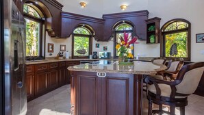 Una cocina amplia con armarios de madera oscura, una isla central con asientos y ventanas grandes que dejan entrar luz natural.