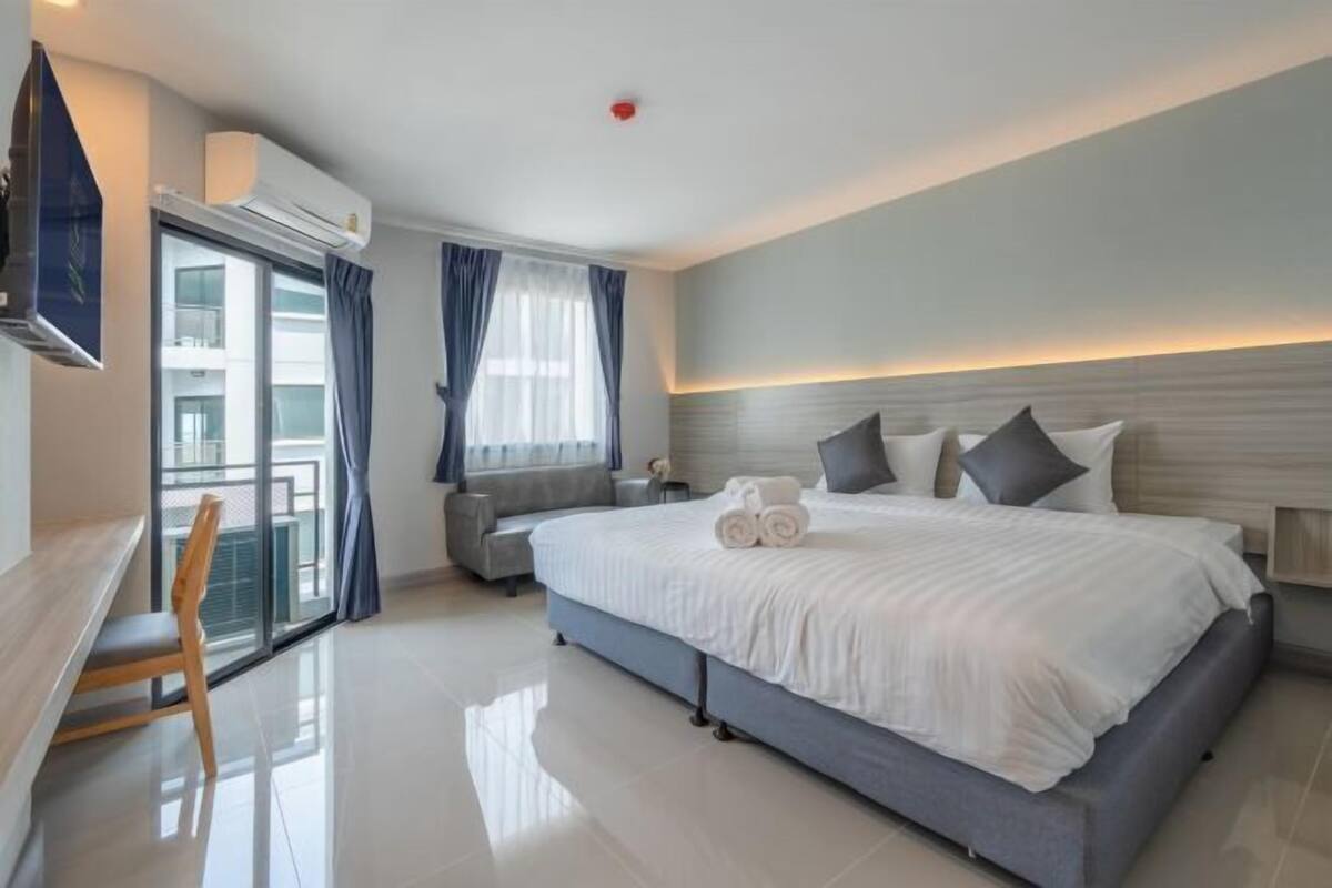 Ein modernes Hotelzimmer mit einem großen Bett, einem Schreibtisch, einem Stuhl und einem Balkon mit Vorhängen.