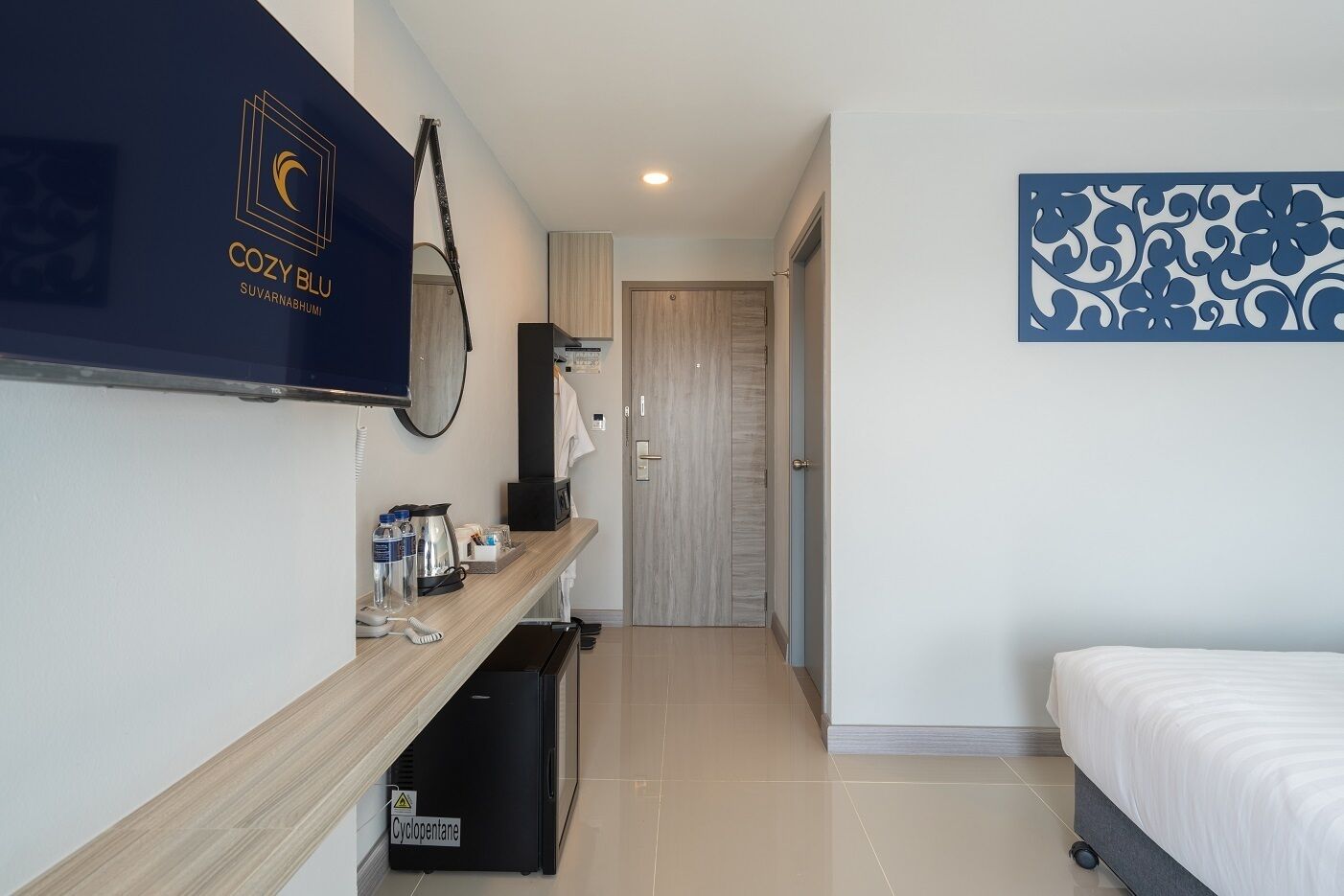 Une chambre d’hôtel avec un lit, un téléviseur fixé au mur, une petite kitchenette équipée d’une machine à café et une porte donnant sur une autre pièce.