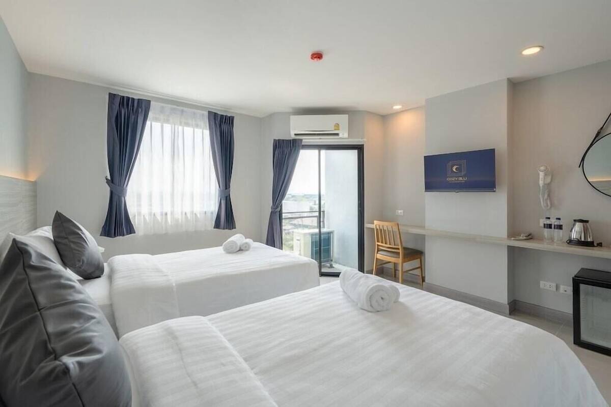Ein Hotelzimmer mit zwei Betten, einem Fernseher, einem Schreibtisch mit Stuhl und einem Balkon.