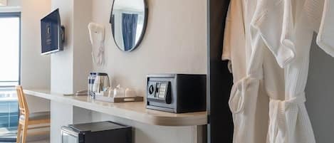 Habitación de hotel con escritorio, espejo, teléfono, radio y bata colgada en la pared.
