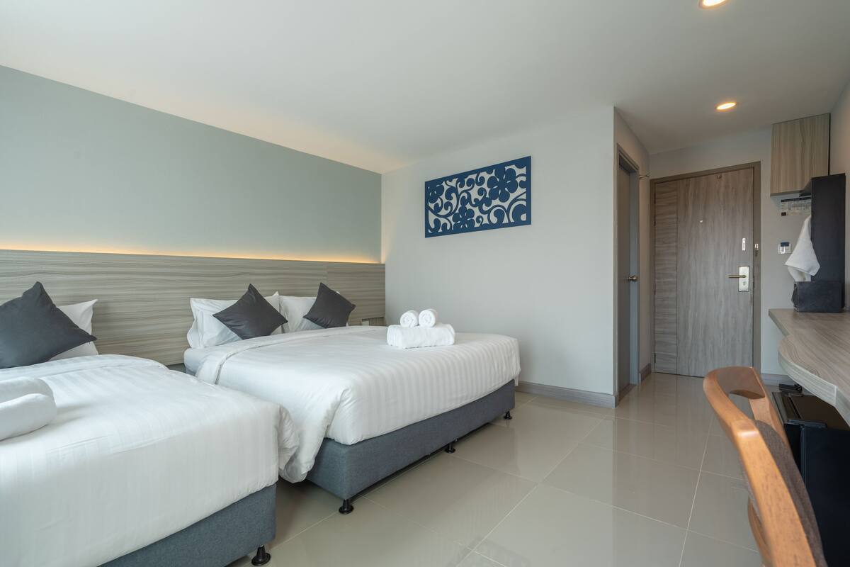 Ein Hotelzimmer mit zwei Betten, einem hölzernen Kopfteil, einem Wandbild und einem durchgegangene Tür erkennbaren Badezimmer.