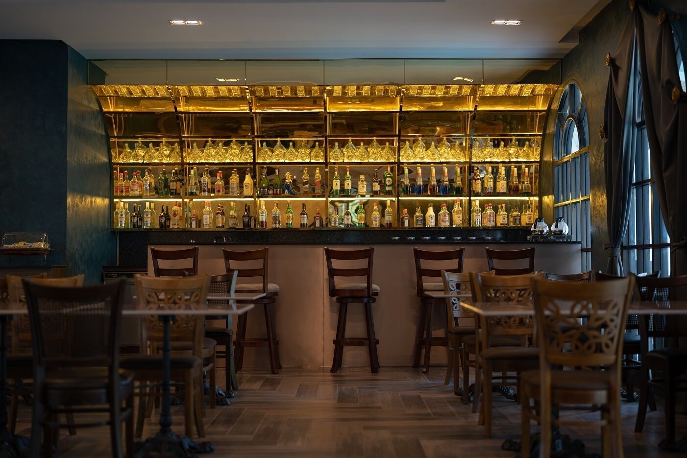 Zona de bar con varias estanterías llenas de botellas, sillas de madera y una barra.