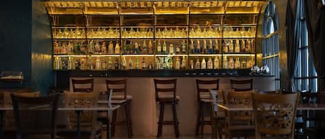 Zona de bar con varias estanterías llenas de botellas, sillas de madera y una barra.