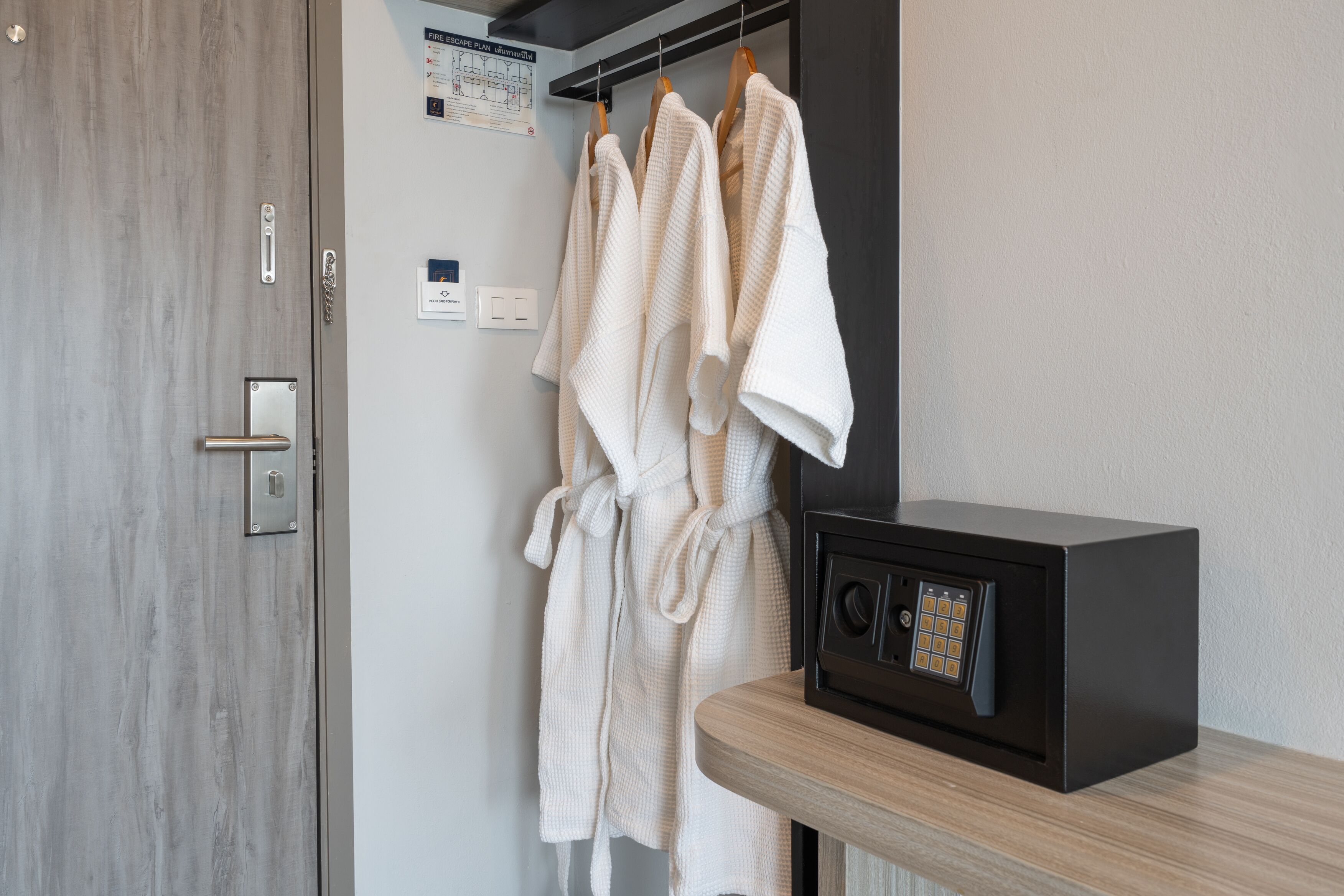 A bathroom with a wooden door, a towel rack with white robes, and a black safe on a wooden counter.