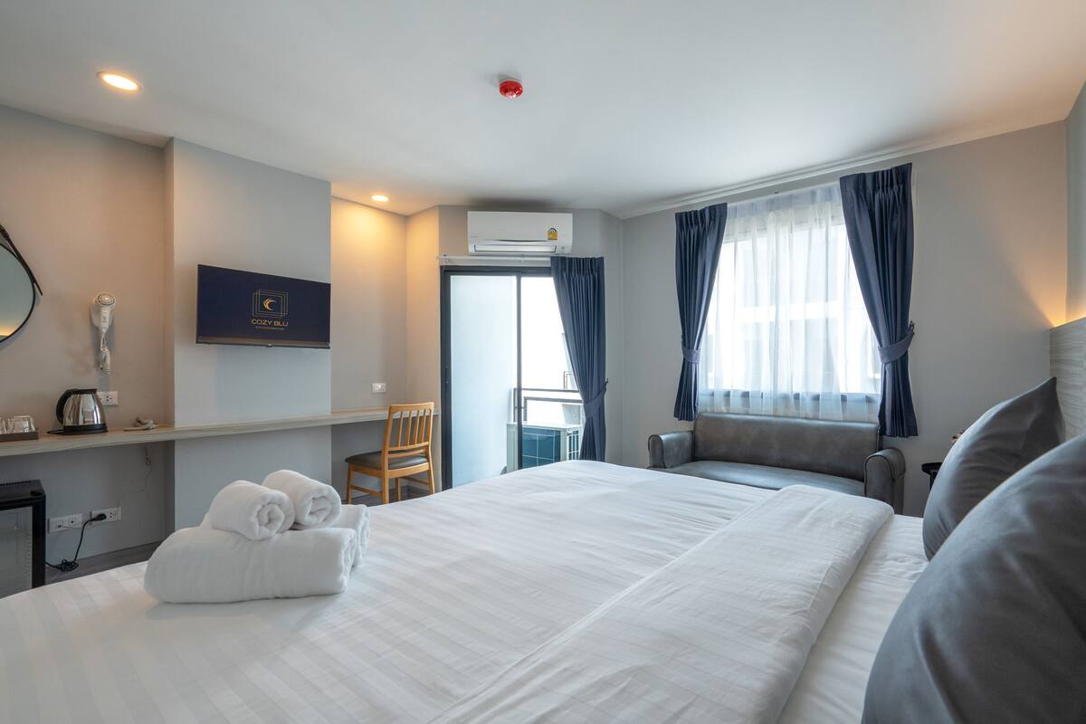 Ein Hotelzimmer mit einem großen Bett, einem Schreibtisch mit Stuhl, einem Fernseher und einem Fenster mit Vorhängen.