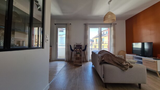 Una sala de estar moderna con sofá, televisor y comedor con sillas y mesa.