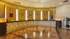 Zona de recepción de un hotel con un mostrador curvo, una recepcionista y cuadros en la pared.