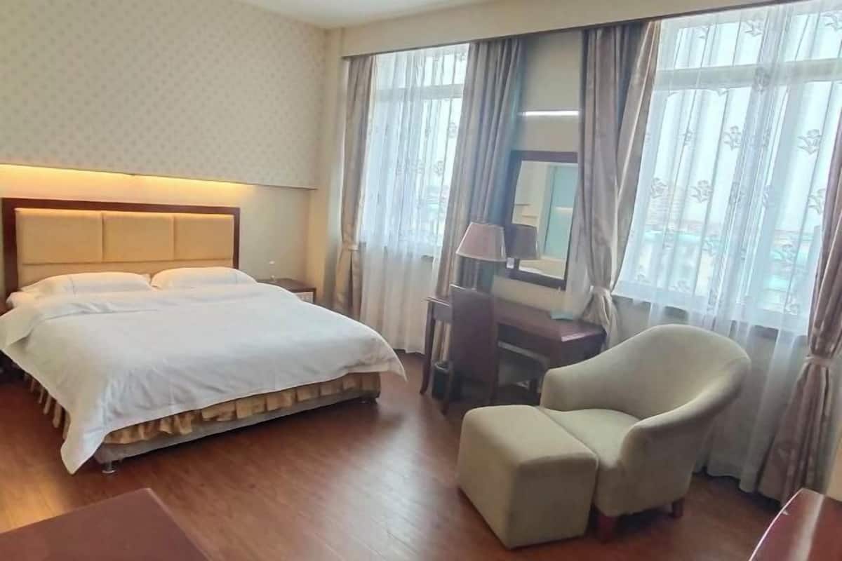 A hotel room with a bed, a chair, a desk, and a window with curtains.