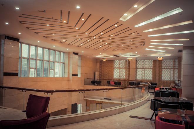 A modern interior with a curved glass railing, a seating area with tables, and a ceiling with linear light fixtures.