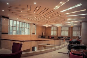 A modern interior with a curved glass railing, a seating area with tables, and a ceiling with linear light fixtures. - Kaixuanmen Hotel (Kaiping)
