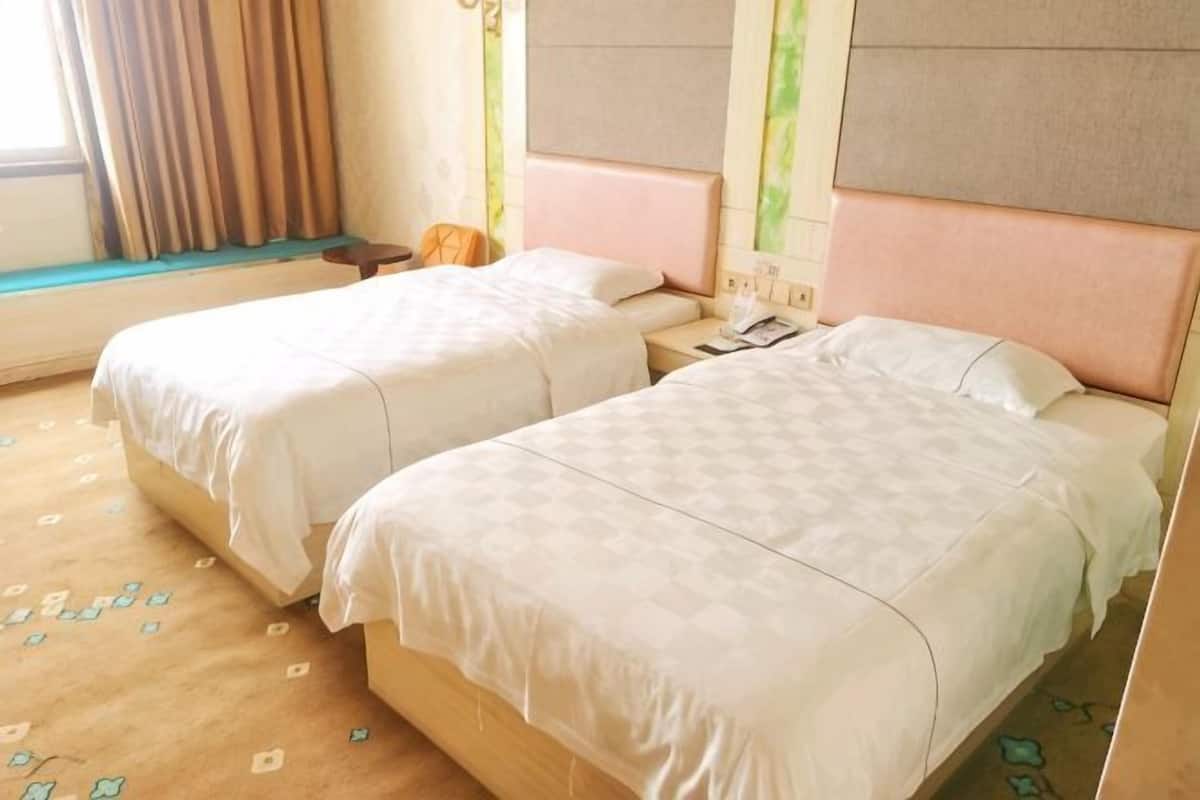 A hotel room with two beds, a nightstand, a lamp, and a window with curtains.