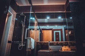 A modern bathroom with a glass-enclosed shower, a large mirror, and a marble countertop.