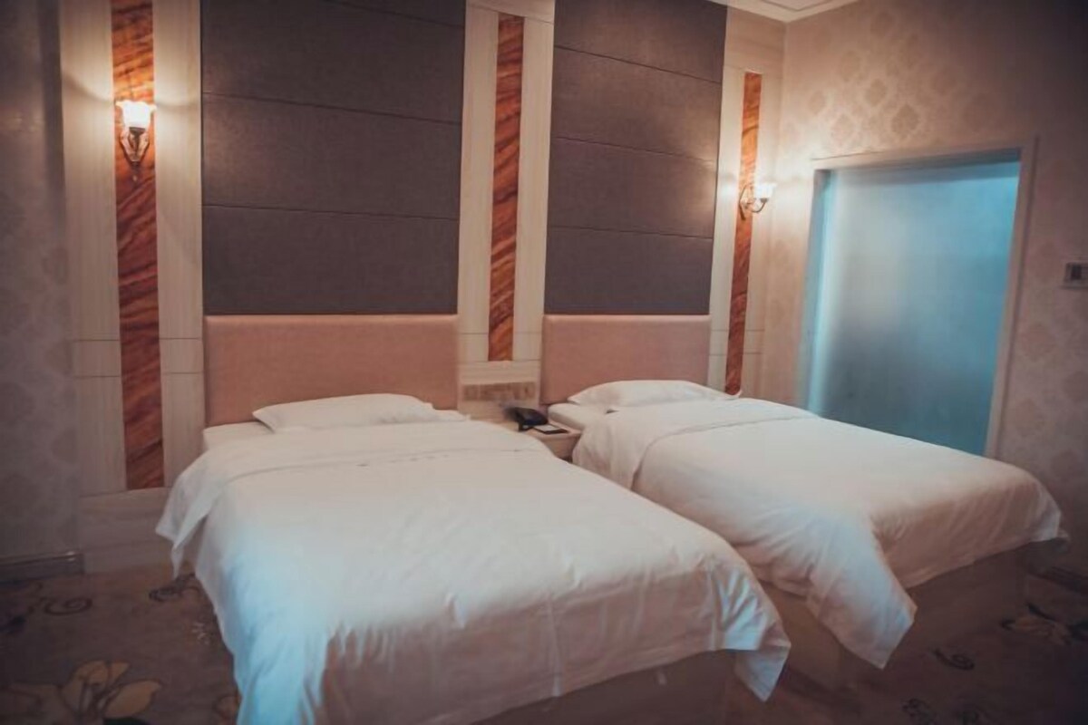 A hotel room with two single beds, a bedside table with a lamp, and a door with a blue handle.
