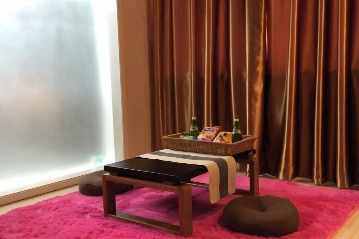 A room with a small table, a basket of snacks, a bean bag, and a window with curtains.