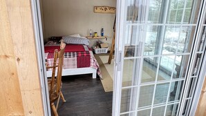 Una habitación con una cama, una silla y una pequeña mesa. Hay una ventana y una puerta.