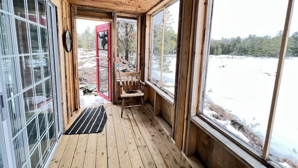 Una cabaña de madera con ventanas amplias, un banco y vista a un paisaje nevado.