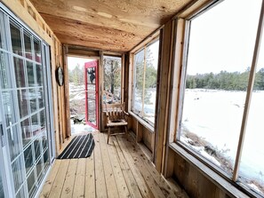 A wooden cabin with large windows, a bench, and a view of a snowy landscape. - Cute off grid Bunkie (Marmora)