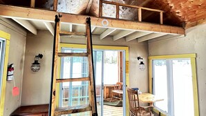 Una habitación estilo loft con techo de madera, una cama en altillo, una escalera, un escritorio y una silla.