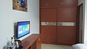 A bedroom with a wooden wardrobe, a television on a wooden stand, and a painting on the wall. - Xifengkezhan (Wuyuan)