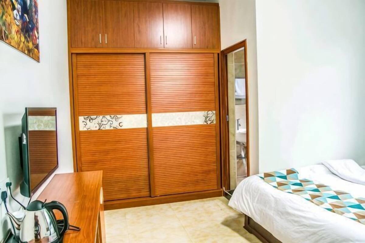 Un dormitorio con un armario de madera, una cama con ropa de cama estampada, un escritorio con espejo y un televisor.