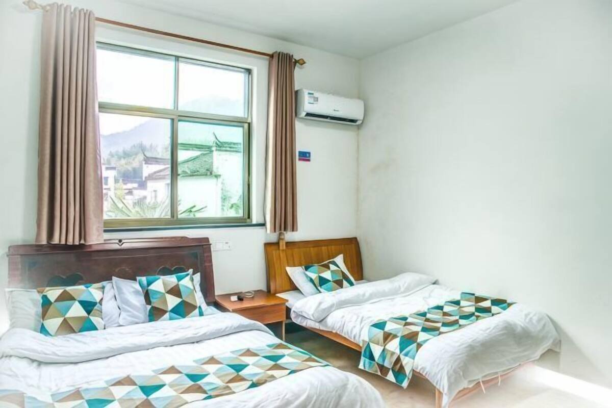 Habitación de hotel con dos camas, una ventana con cortinas, un equipo de aire acondicionado y vista a una montaña.