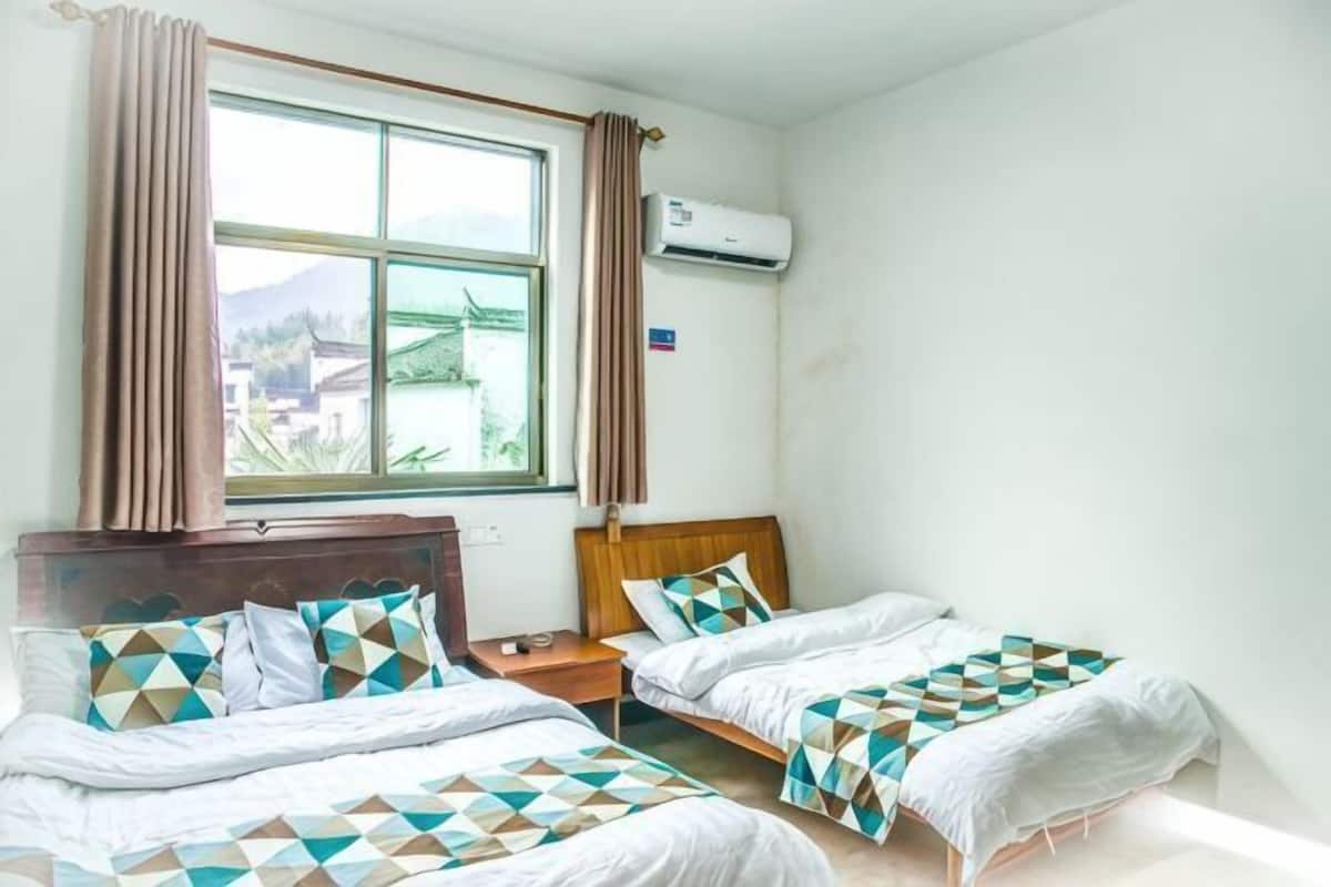 A hotel room with two beds, a window with curtains, an air conditioning unit, and a view of a mountain.