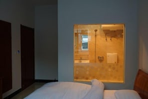 A bedroom with a bed, a window with a view of a bathroom, and a door. - Xifengkezhan (Wuyuan)