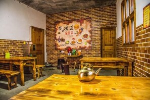 A room with brick walls, wooden tables, and benches. There is a poster on the wall and a kettle on one of the tables. - Xifengkezhan (Wuyuan)