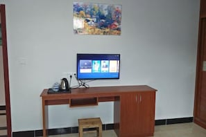 A room with a wooden desk, a television mounted on the wall, a small stool, and a painting above the desk. - Xifengkezhan (Wuyuan)
