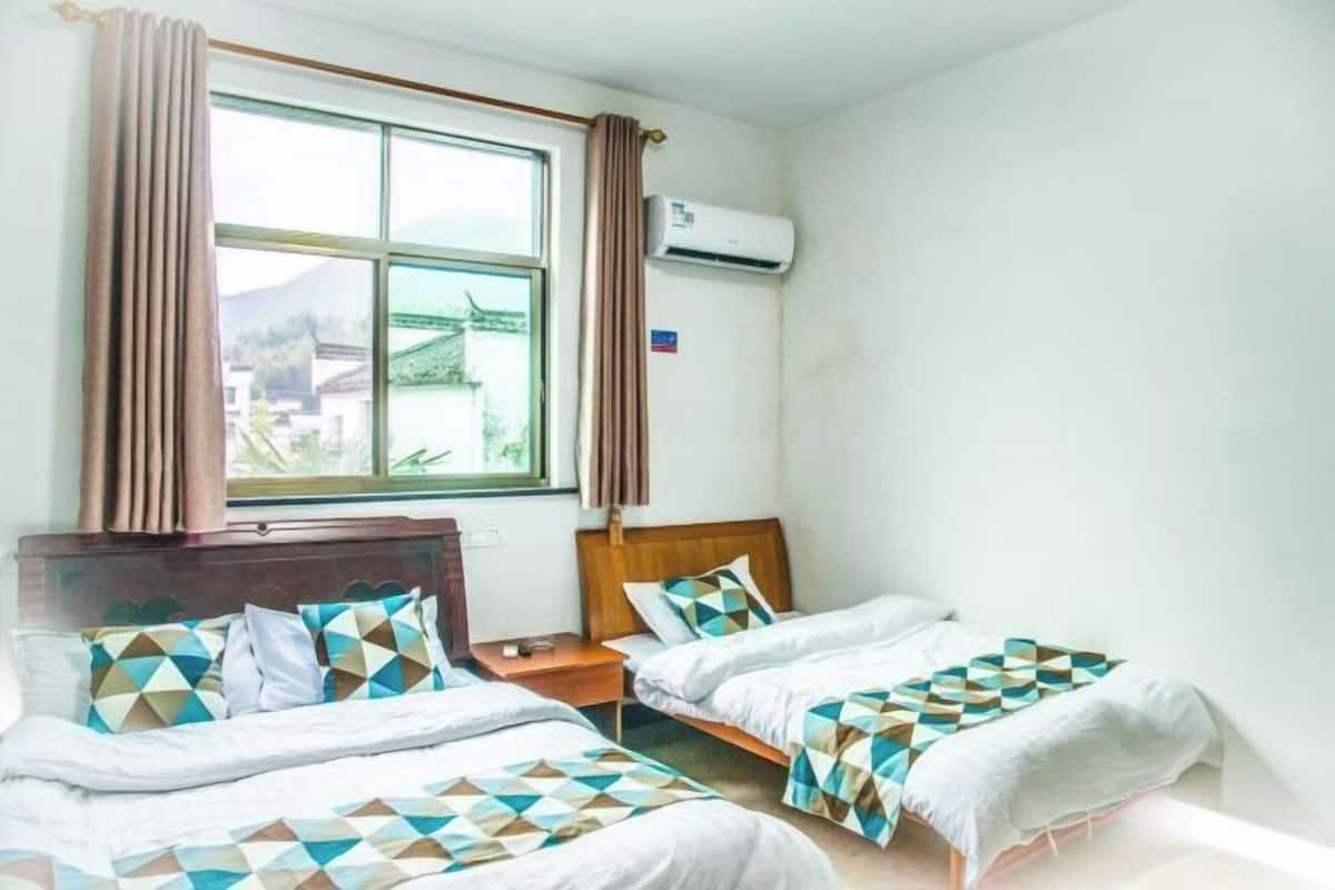 Habitación de hotel con dos camas, una ventana con cortinas, un equipo de aire acondicionado y vista a un edificio.