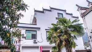 A two-story building with a white facade, a visible air conditioning unit, and a palm tree in the foreground. - Xifengkezhan (Wuyuan)
