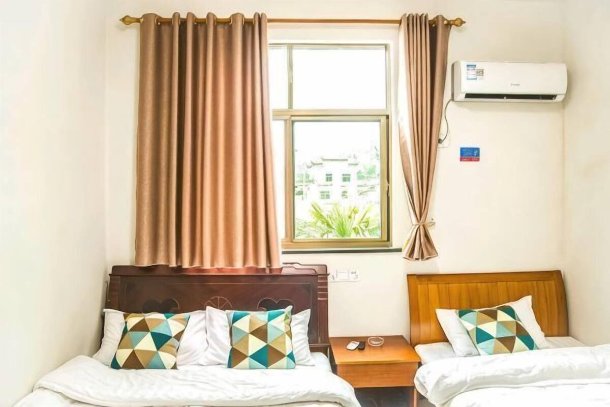 Habitación de hotel con dos camas, una ventana con cortinas, un equipo de aire acondicionado y una mesita con teléfono.