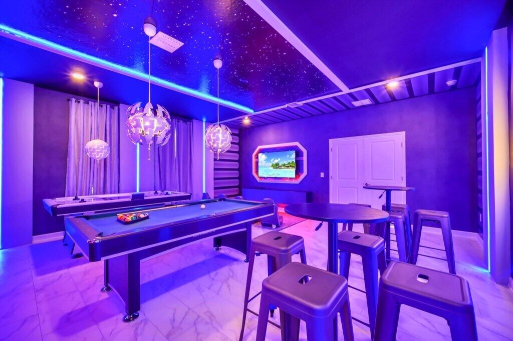 A pool table with stools, a television, and a ceiling with a starry design.