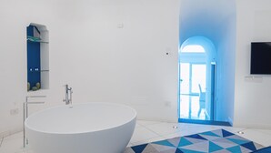Ein modernes Badezimmer mit einer großzügigen, freistehenden Badewanne, einer integrierten Ablagefläche mit Pflegeprodukten und einem geometrisch gemusterten Teppich.